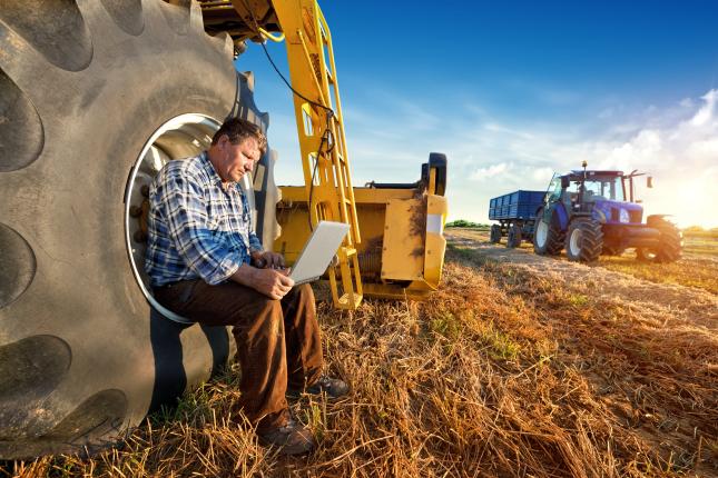 Man sitting next to farm equipment and working on a laptop.